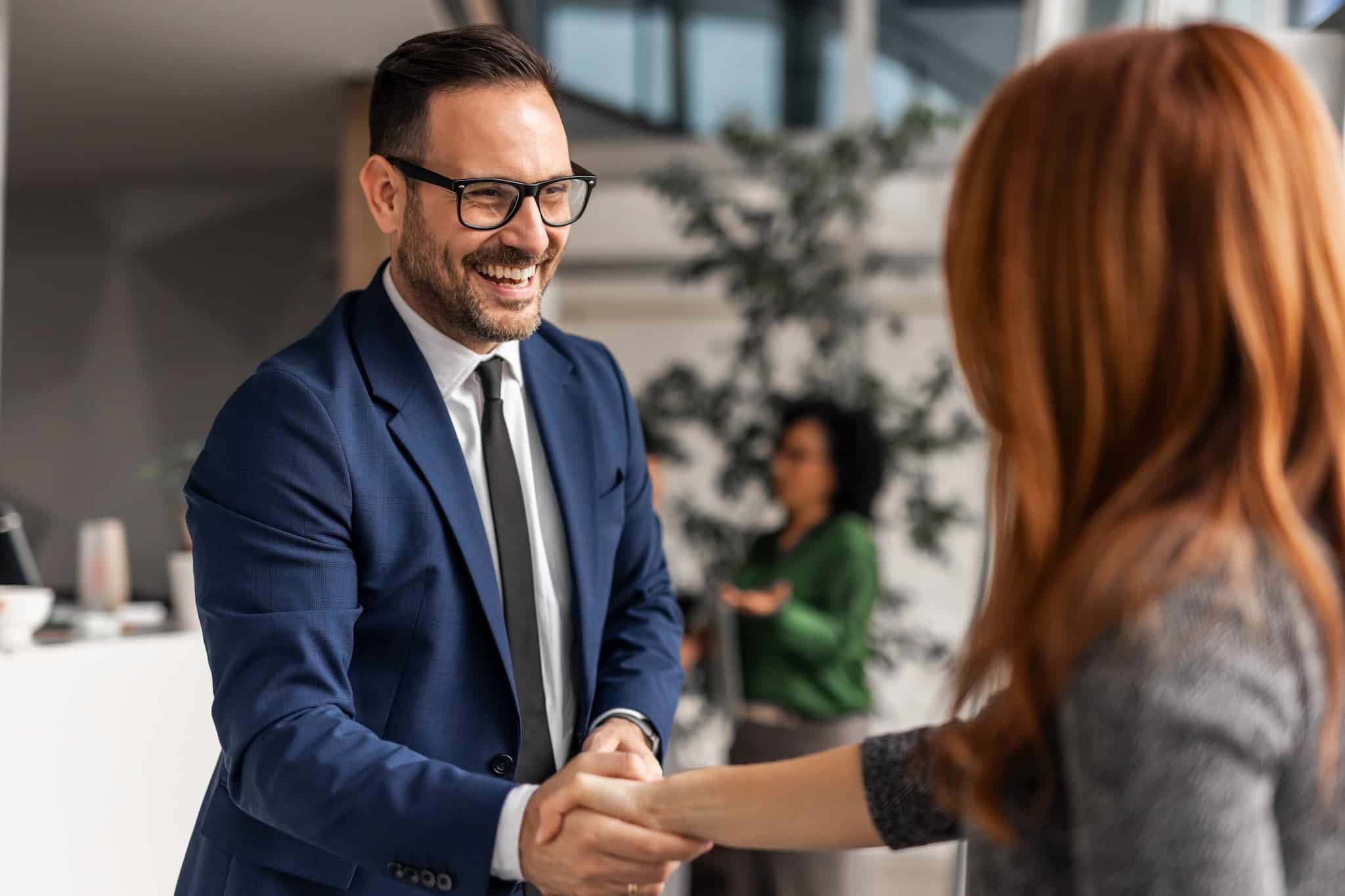 Two professionals warmly shaking hands in a modern office environment, showcasing collaboration and positive interactions. A vibrant and friendly ambiance highlights teamwork and success.