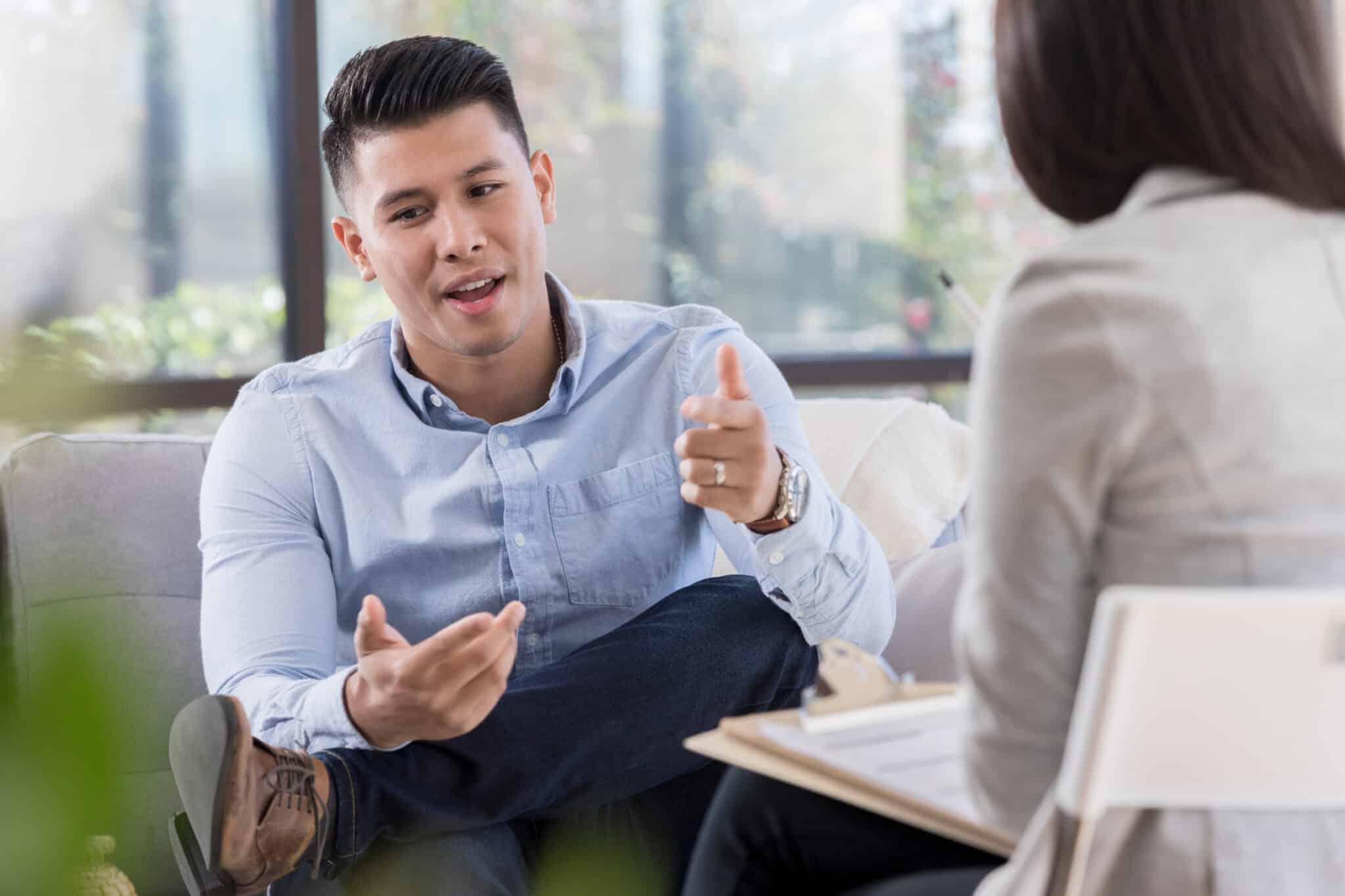 Thirtysomething man sharing thoughts while interviewer listens and takes note on a clipboard
