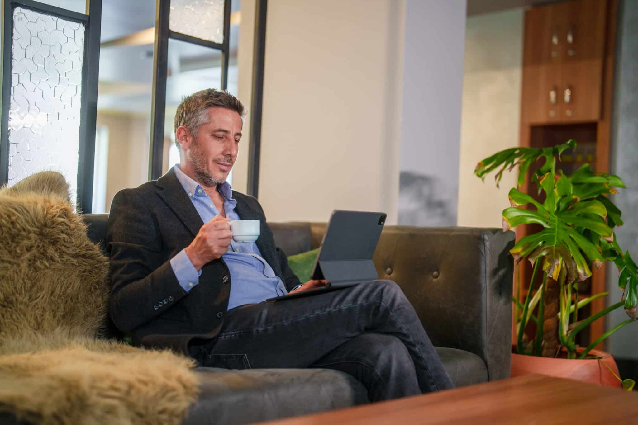 Middle aged man on computer holding a cup of coffee having a client feedback conversation
